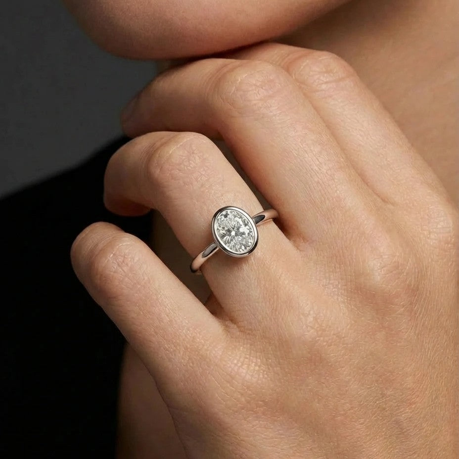 Model wearing oval cut diamond ring in solid gold with bezel setting and timeless minimalist design