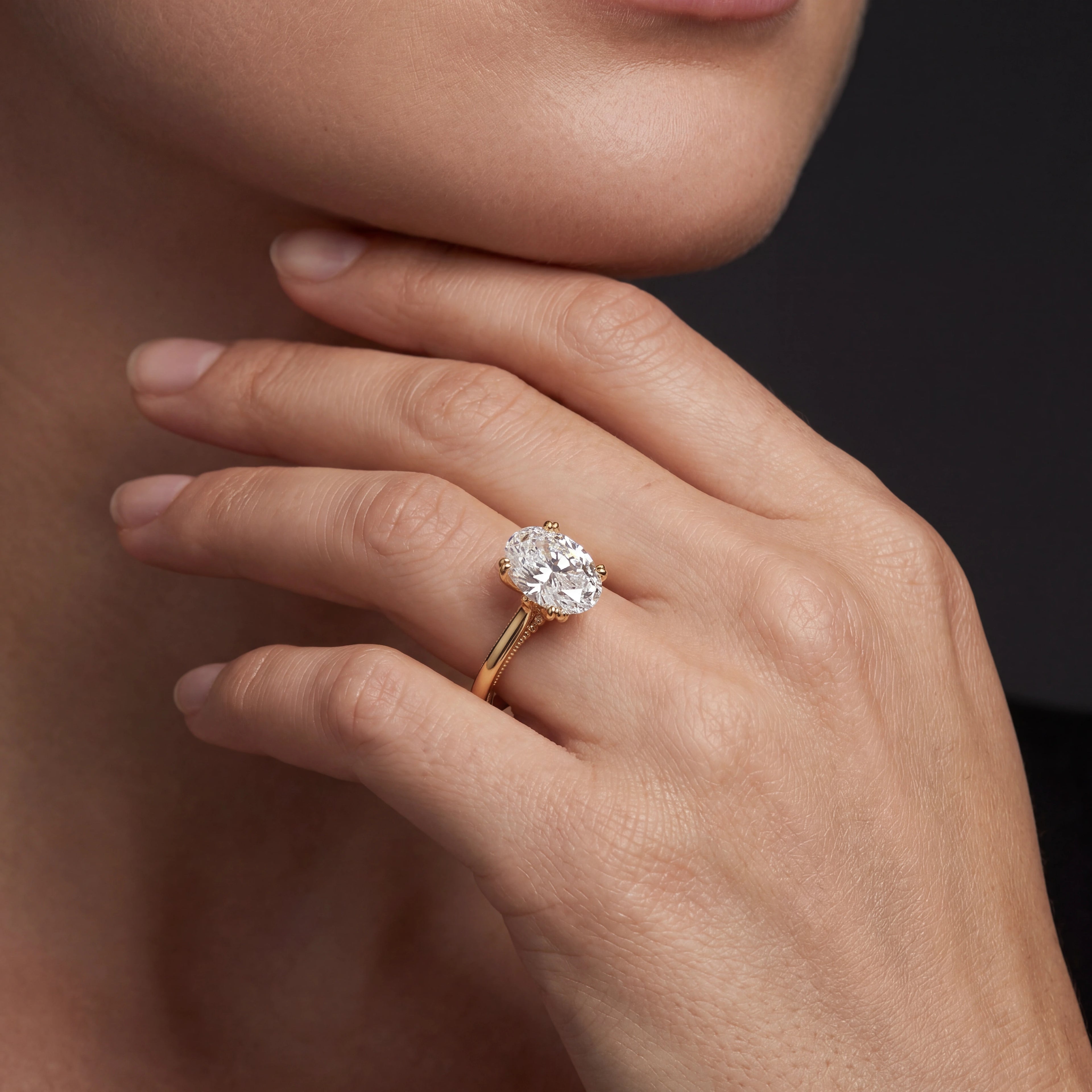 Model wearing oval cut lotus prong milgrain Lab-Grown Diamond engagement ring in 14K yellow gold, close-up showing petal prong setting and gallery detail — Black Pearl of Queens