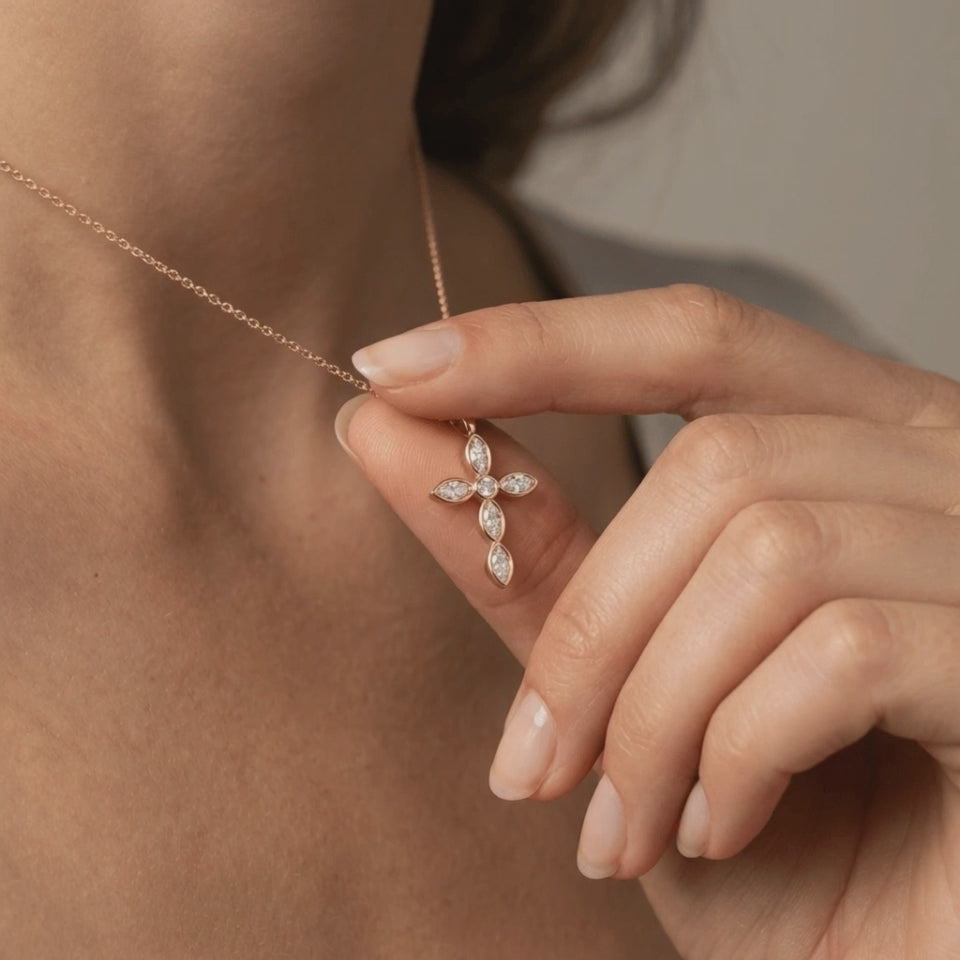 Woman gently holding 14K gold marquise diamond cross pendant with round center diamond