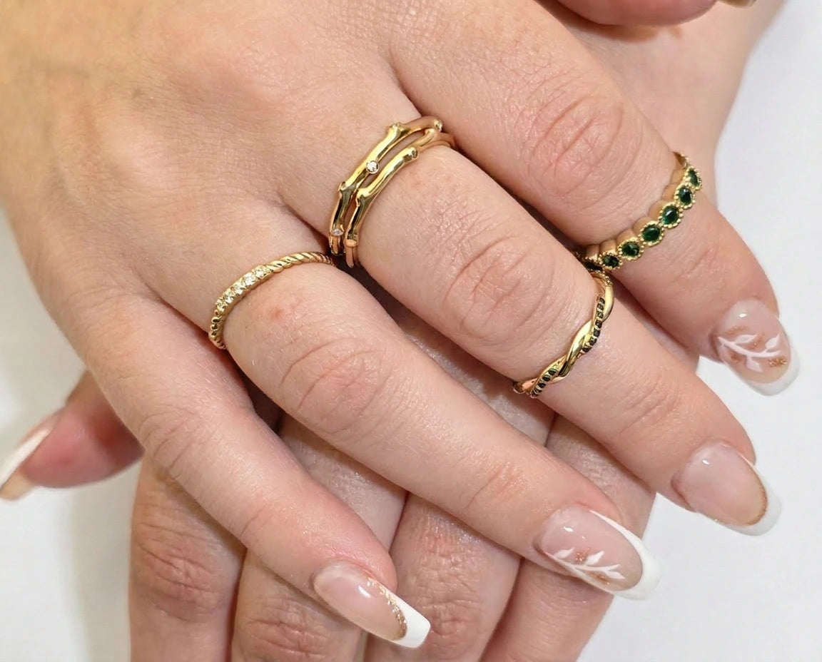 Close-up of fingers wearing gold rings with green gemstones on a neutral background