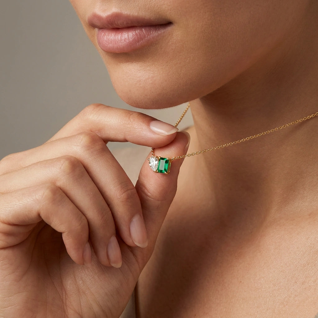 Woman wearing pear diamond and emerald Toi et Moi necklace in yellow gold