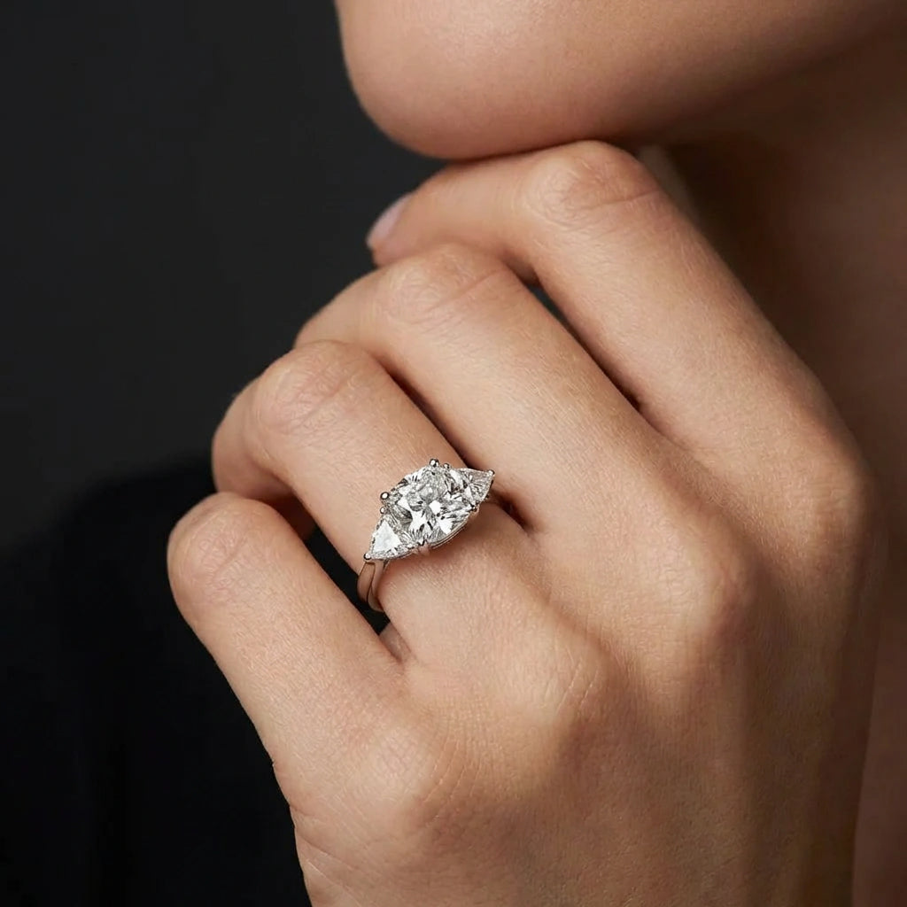 Close up of Vela trilogy diamond engagement ring showing round brilliant center diamond and pear side stones in prong setting