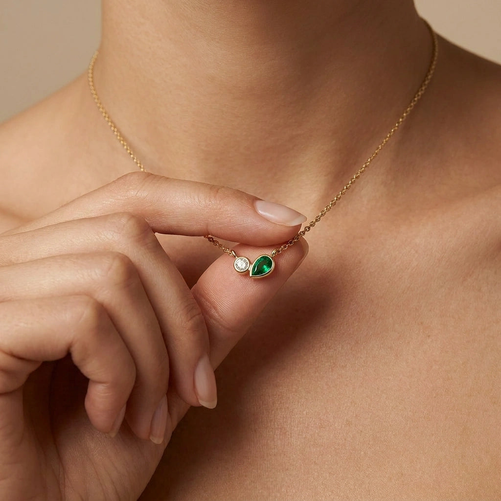 Woman wearing minimalist diamond and pear emerald necklace in yellow gold