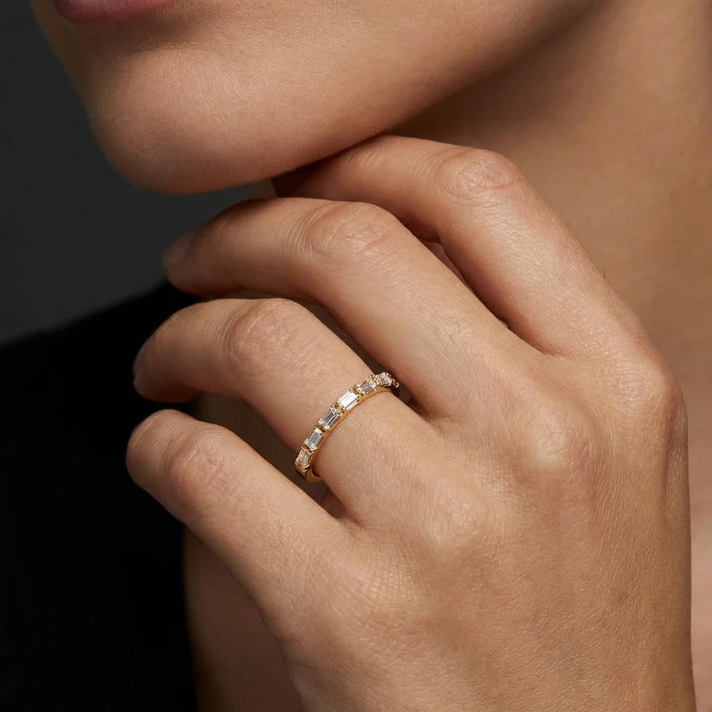 Female model wearing Virel Baguette Diamond Half Eternity Band in 14K yellow gold, close-up editorial shot showing horizontal baguette diamonds across top of band on finger