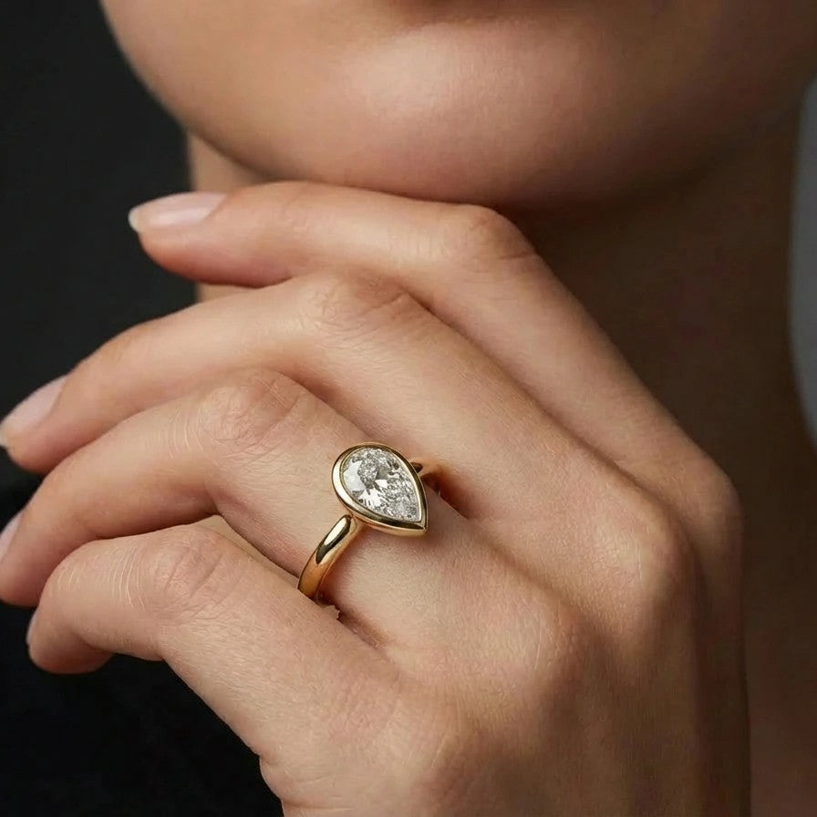 Model wearing pear cut diamond ring in solid gold with bezel setting and elegant minimalist design