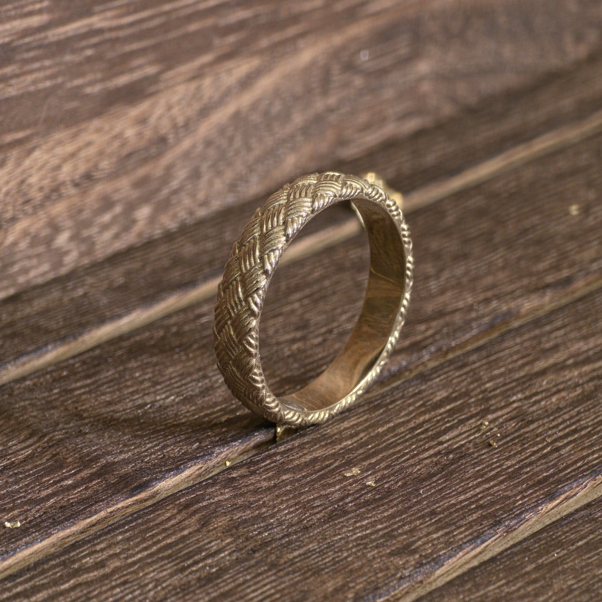 Handcrafted woven gold wedding ring photographed on wooden background
