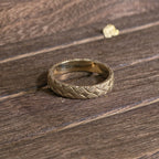 Close-up of woven gold ring with detailed basket weave texture on wooden surface