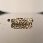 Close-up of woven gold ring with detailed basket weave texture on reflective surface