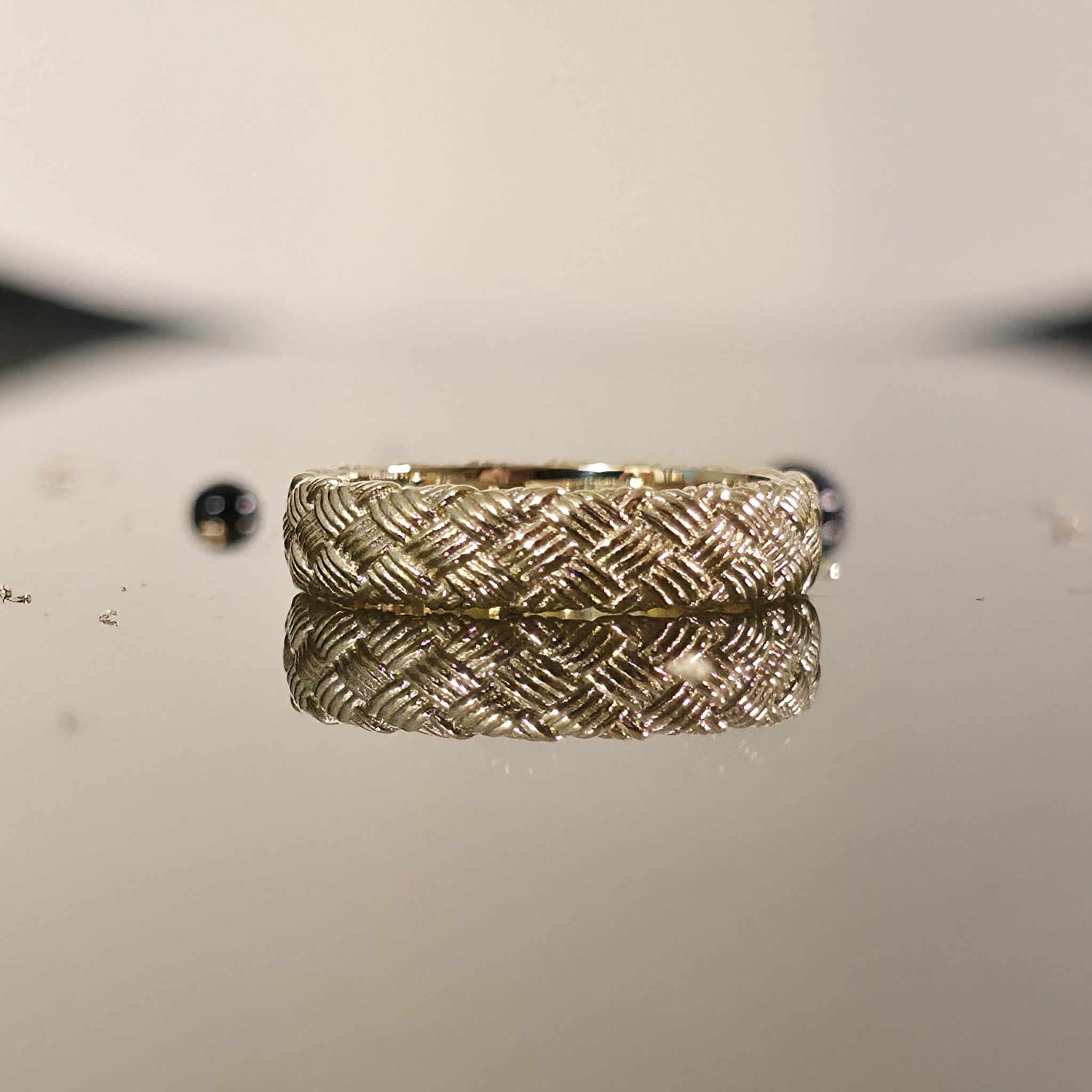 Close-up of woven gold ring with detailed basket weave texture on reflective surface