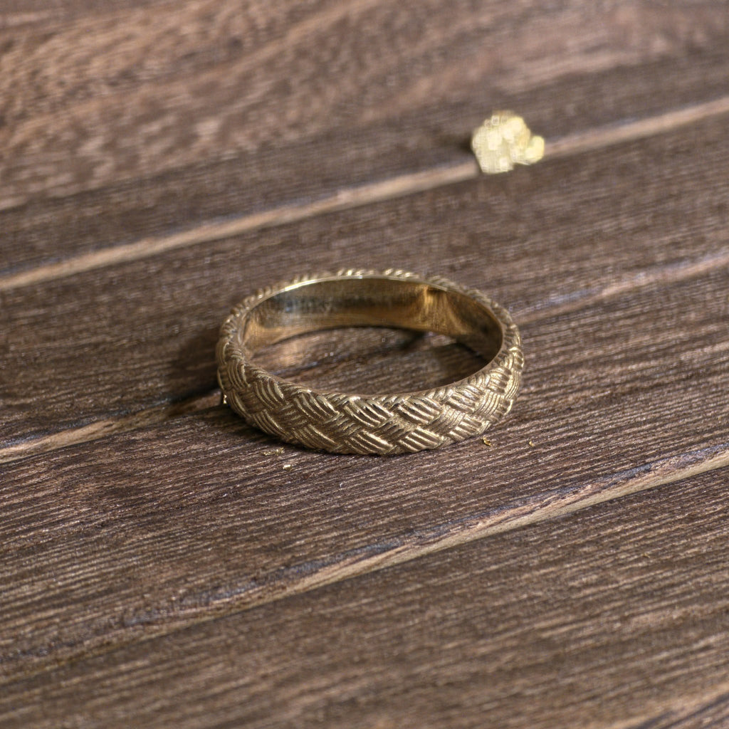 Close-up of woven gold ring with detailed basket weave texture on wooden surface