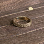 Close-up of woven gold ring with detailed basket weave texture on wooden surface