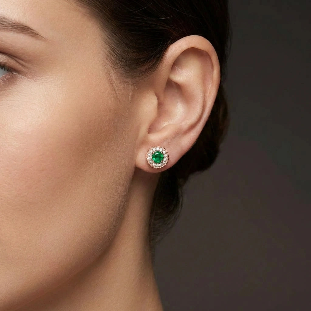 Woman wearing Zirelle emerald halo stud earrings in rose gold with round green emerald center and diamond halo